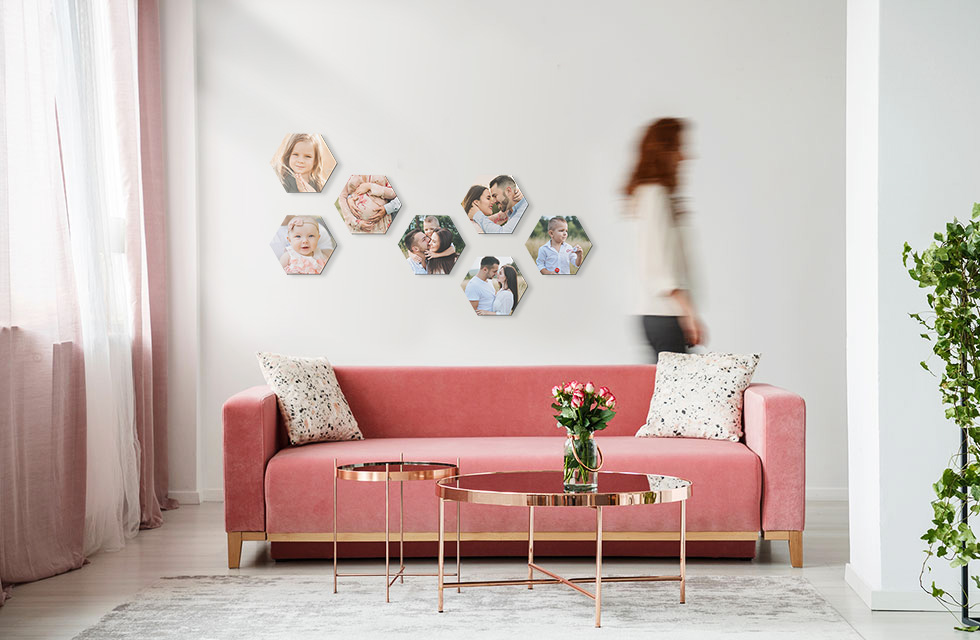 Woman walks by a set of multiple Snapfish Photo Tiles in a checked pattern on a wall featuring family photos above a pink sofa